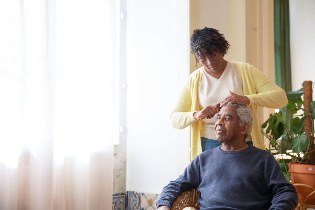 Free A caregiver combing an elderly man's hair near a sunlit window indoors. Stock Photo