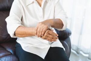 Elderly woman sitting on a couch holding her shaking hand, showing signs of hand tremors.