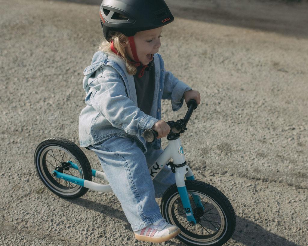 Toddler riding a Biky balance bike in a traffic-free paved area